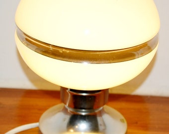 May include: A white globe lamp with a chrome base and a gold band around the middle. The lamp is on a wooden surface.