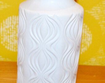 May include: White ceramic vase with a textured, wavy design. The vase has a wide mouth and a narrow base.
