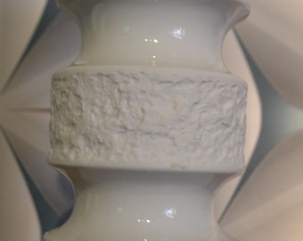 May include: White ceramic vase with a textured surface. The vase has three sections, each with a different height. The vase is a modern design.