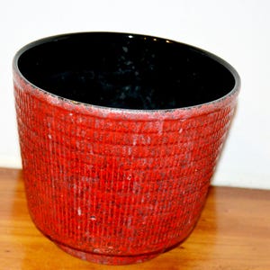 Può includere: Un vaso di terracotta rosso con interno nero e un motivo testurizzato intrecciato. Il vaso è alto circa 18 cm e largo 20 cm.