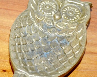 May include: A brass owl trinket dish with a detailed design. The owl has large eyes and a textured body.