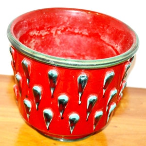 May include: Red ceramic planter with a green rim and a textured design of teardrop shapes.