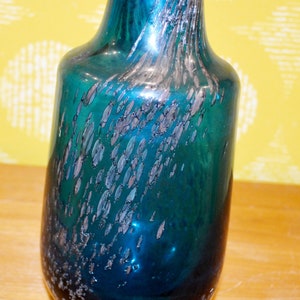 May include: A teal blue glass vase with silver flecks throughout. The vase has a rounded body and a narrow neck.