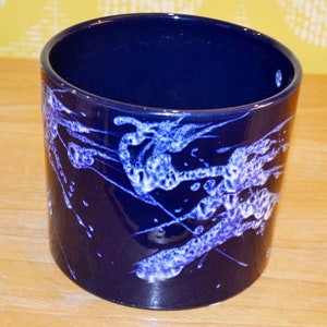 Könnte beinhalten: Ein dunkelblauer Keramiktopf mit einem weißen und hellblauen abstrakten Design. Der Topf ist zylindrisch und hat eine glatte, glänzende Oberfläche.