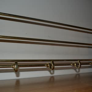 May include: A wall-mounted coat rack with three brass rails and five hooks. The rack is made of wood with a light brown finish.