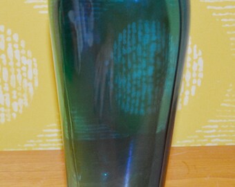 Könnte beinhalten: Eine hohe, schlanke Vase mit einem Teal-Blau- bis Grün-Verlauf. Die Vase hat einen klaren Glasboden.