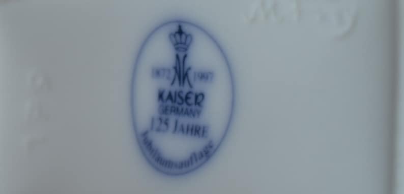 Puede incluir: Un sello de porcelana azul y blanco con una corona y el texto "1872 K 1907 Kaiser Germany 125 Jahre Jubilaums Auflage".