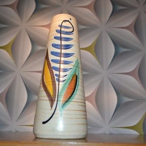 May include: A white ceramic vase with a tall, slender shape and a geometric pattern of brown, blue, yellow, and green leaves.