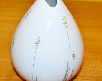 May include: A white ceramic vase with a teardrop shape and a narrow opening. The vase has a simple design with gray lines and yellow dots, resembling stylized grass.