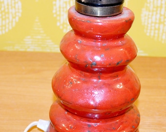 Könnte beinhalten: Eine rote Keramik-Tischlampe mit einem schwarzen und goldenen Metallfuß. Die Lampe hat eine strukturierte, leicht gesprenkelte Oberfläche.