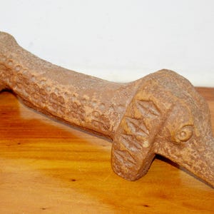 May include: A brown, carved sculpture of a dachshund dog. The dog is lying down, with its head and tail raised slightly. The sculpture has a textured surface and is resting on a wooden surface.