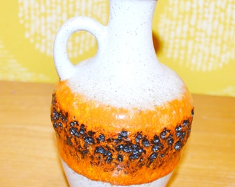May include: A white ceramic vase with a speckled glaze and a black rim. The vase has a wide, round body and a narrow neck. The vase is decorated with a band of orange glaze with black speckles around the middle.