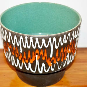 May include: A brown ceramic planter with a teal glaze inside. The planter has a white and orange wavy design around the outside.