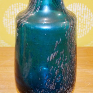 May include: A teal blue glass vase with a textured, speckled finish. The vase has a rounded body and a narrow neck.