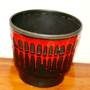Könnte beinhalten: Ein schwarzer und roter Keramiktopf mit einem Tropf-Glazureffekt. Der Topf hat eine breite, runde Öffnung und einen leicht ausgestellten Boden.