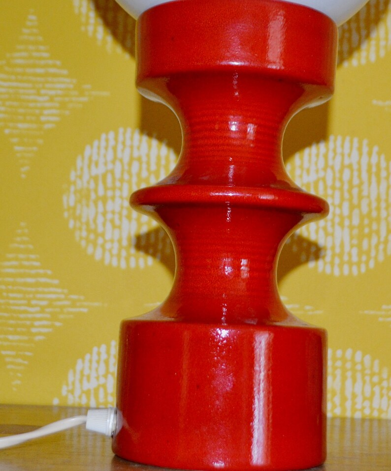 May include: A red ceramic table lamp with a white globe shade. The lamp has a unique, tiered base.