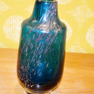 May include: A teal blue glass vase with silver flecks throughout. The vase has a round body and a narrow neck.