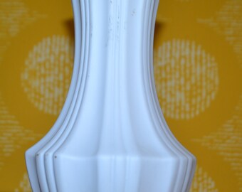 Puede incluir: Un jarrón de cerámica blanco con un diseño acanalado. El jarrón tiene un cuello estrecho y una base ancha.