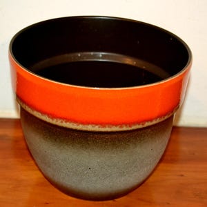 Könnte beinhalten: Ein großer, runder, orangefarbener und brauner Keramiktopf. Der Topf hat eine breite, runde Öffnung und einen abgerundeten Boden. Der Topf ist in einem dunklen Braun glasiert mit einem Band aus orangefarbener Glasur um den oberen Rand.