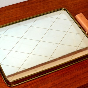 Könnte beinhalten: Rechteckiges Serviertablett mit verspiegelter Oberfläche und goldfarbenem Metallrahmen. Der Spiegel hat ein Rautenmuster. Das Tablett hat Holzgriffe an jedem Ende. Das Tablett steht auf einer Holzoberfläche.