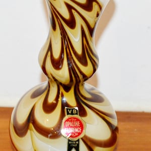 Może przedstawiać: Dekoracyjny szklany wazon z pękatą podstawą i rozszerzaną górą. Wazon ma wirujący wzór w kolorach brązowym i beżowym. Etykieta głosi "OPALINE FLORENCE" i "MADE IN ITALY".