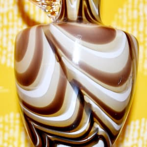 Może przedstawiać: Wazon ze szkła w brązowo-białe pasy z przezroczystym szklanym uchwytem. Wazon ma wzór spiralny.