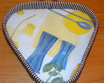 May include: A heart-shaped serving tray with a white and brown striped rim. The tray has a white background with a colorful design featuring blue glasses, yellow circles, and a green plant.