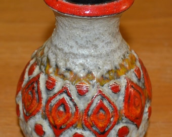 May include: A small, white ceramic vase with a red rim and a geometric pattern in shades of orange and red. The vase has a textured surface and a black interior.