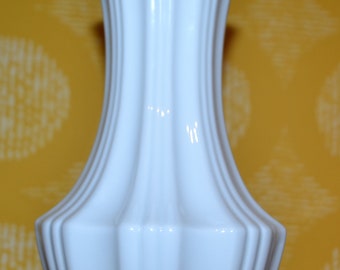Puede incluir: Un jarrón de cerámica blanco con un diseño acanalado. El jarrón tiene un cuello estrecho y una base ancha.