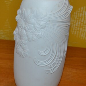 May include: White ceramic vase with a raised floral design. The vase is oval shaped and has a smooth, glossy finish.