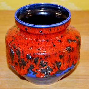 Może przedstawiać: Niebiesko-pomarańczowy ceramiczny wazon z efektem glazury kropelkowej. Wazon ma szeroki otwór i zaokrąglone ciało.