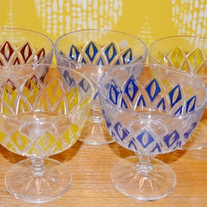 Puede incluir: Cinco copas de postre de vidrio transparente con un patrón geométrico en tonos de amarillo, azul y rojo. Las copas tienen un borde festoneado y un tallo corto.