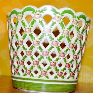 May include: White ceramic planter with a green lattice design and pink floral accents. The planter has a scalloped top and a green base.