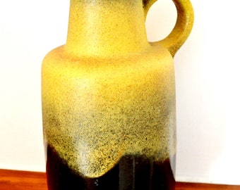 May include: A yellow and brown ceramic vase with a wide mouth and a handle. The vase has a mottled glaze and a dark brown base.