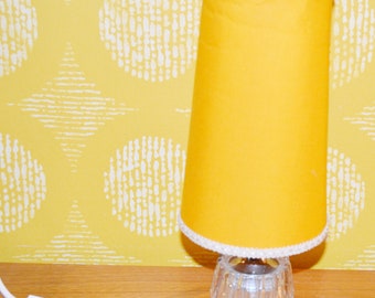 May include: A yellow table lamp with a white trim on the shade and a clear glass base.
