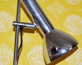 May include: A silver adjustable floor lamp with a long, slender arm and a round, reflective shade. The lamp is on a yellow background with a white pattern.