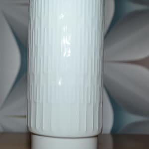 Könnte beinhalten: Weiße Keramikvase mit geometrischem Muster. Die Vase hat eine zylindrische Form mit einem breiten Boden.
