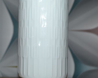 Puede incluir: Jarrón de cerámica blanco con un patrón geométrico. El jarrón tiene una forma cilíndrica con una base ancha.