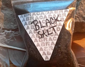 May include: A close-up of a small bag of black salt with a white triangle label that says "BLACK SALT" and is surrounded by the word "ABRACADABRA".