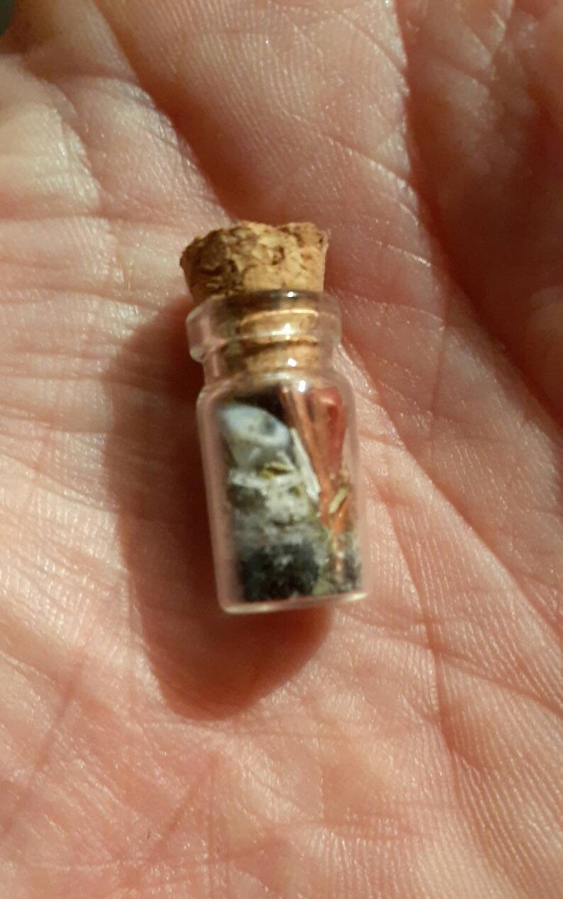 May include: A small glass bottle with a cork stopper filled with various small objects, including a white shell, a piece of red coral, and other small pieces of sea glass.