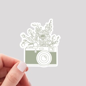 Puede incluir: Un dibujo de l&iacute;nea verde de una c&aacute;mara vintage con un ramo de flores que se derrama por la parte superior.