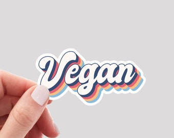 May include: A white sticker with the word "Vegan" in a retro, rainbow-coloured font. The sticker has a white outline and is slightly raised.