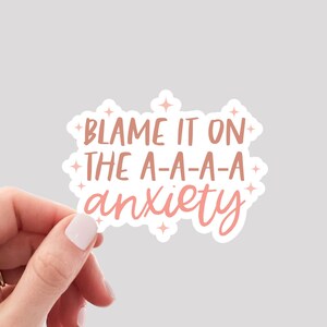 Puede incluir: Pegatina rosa y blanca con el texto "Blame it on the a-a-a-a anxiety" con peque&ntilde;as estrellas alrededor del texto.