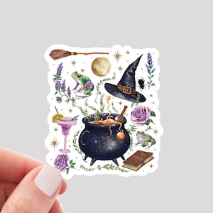 May include: A witchy themed sticker featuring a black cauldron with a bubbling potion, a witch's hat, a frog, a book, a broom, and other magical elements. The sticker is on a white background.