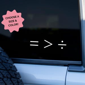 May include: A black car window with a white graphic of mathematical symbols: equals, greater than, and division. A pink starburst shape with the text "CHOOSE A SIZE & COLOR!" is in the upper left corner.