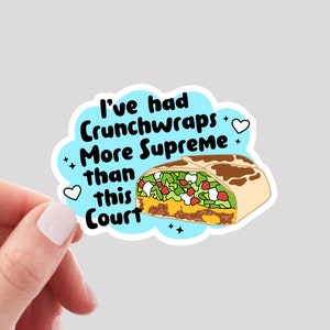 May include: A blue and white sticker with the text "I've had Crunchwraps More Supreme than this Court" and a cartoon image of a taco.