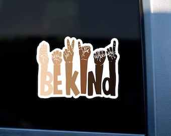 May include: A white sticker with the word "BE KIND" in black letters. The letters are formed by hands in different skin tones signing the letters in American Sign Language.