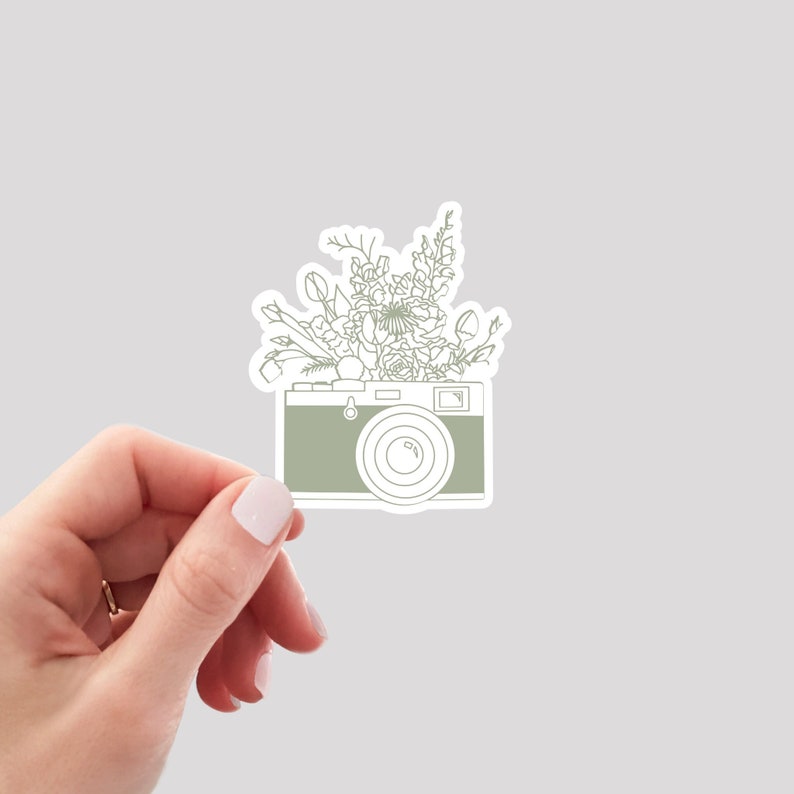 Puede incluir: Un dibujo de l&iacute;nea verde de una c&aacute;mara vintage con un ramo de flores que se derrama por la parte superior.