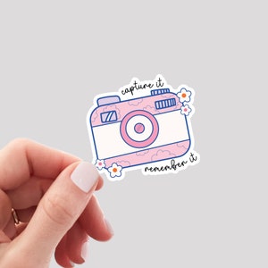 May include: Pink and blue camera sticker with white flowers and the text "capture it remember it".
