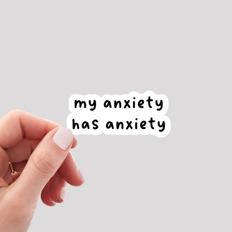 以下が含まれることがあります： 「my anxiety has anxiety」と黒文字で書かれた白いステッカー。手に持たれている。